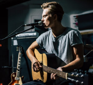 Man with acoustic guitar singing on stage.