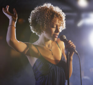 Woman singing on a stage with a spotlight in the background.