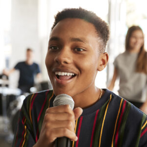Young man singing into a microphone in a classroom setting.